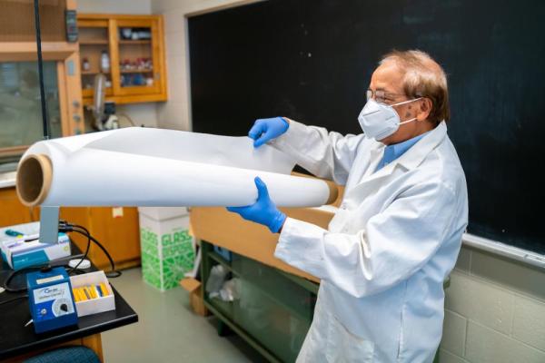 A masked researcher holds a spool of material